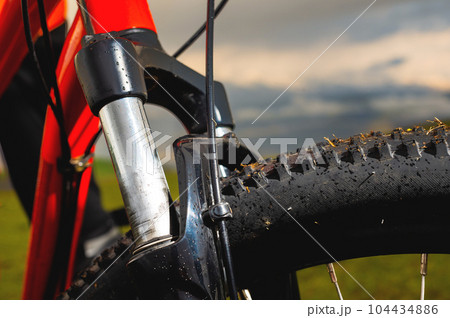 Close-up of bicycle front suspension fork with off-road mountain bike rubber outdoors against sunset clouds and mountains 104434886