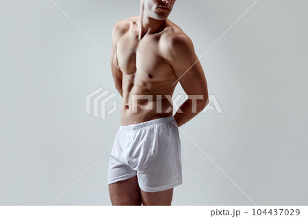 Cropped image of beautiful, muscular, fit, strong male body against grey studio background. Model posing in underwear Cropped image of beautiful, muscular, fit, strong male body against grey studio background. Model posing in underwear 104437029