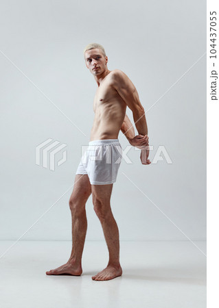 Relief torso. Full-length portrait of handsome young man with blonde hair, muscular body posing in underwear against grey studio background 104437055