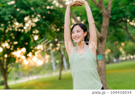Female jogger. Fit young Asian woman with green sportswear stretching muscle in park before running and enjoying a healthy outdoor. Fitness runner girl in public park. Wellness being concept 104438034