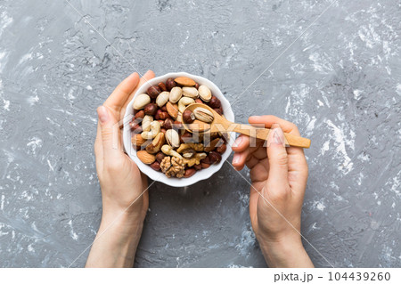 Woman hands holding a wooden bowl with mixed nuts Walnut, pistachios, almonds, hazelnuts and cashews. Healthy food and snack. Vegetarian snacks of different nuts 104439260