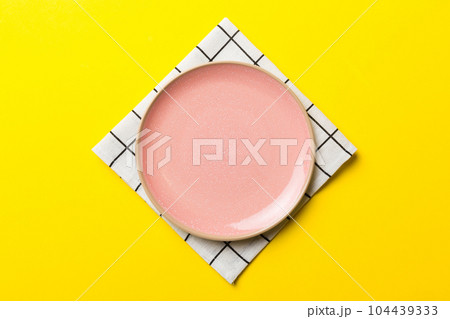 Top view on colored background empty round pink plate on tablecloth for food. Empty dish on napkin with space for your design Top view on colored background empty round pink plate on tablecloth for food. Empty dish on napkin with space for your design 104439333