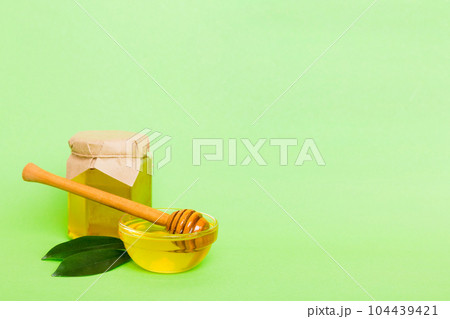 Honey in jar with leaves and honey dipper on colored background top view with copy text 104439421