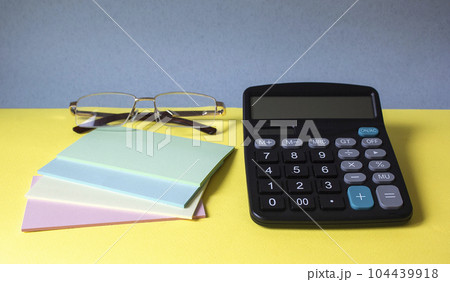 Close-up of a business workplace with colorful stickers, a calculator and glasses 104439918