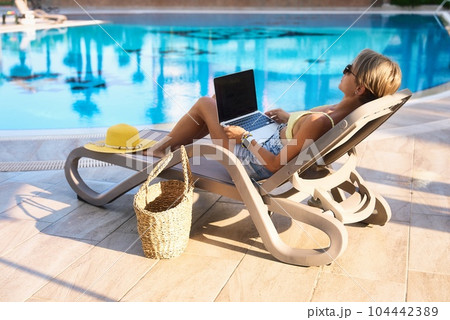 Hipster woman using laptop by the pool. Young girl freelancer working on a laptop while on vacation 104442389