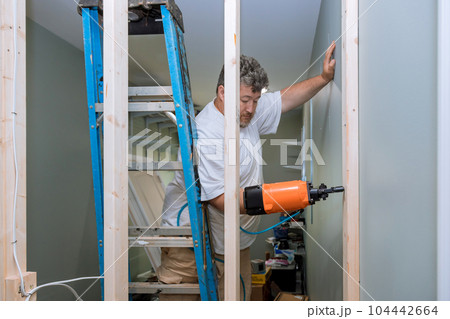 Building home using an air hammer to nail wooden beams framework of house during construction 104442664