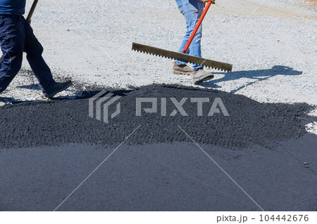 Workmen working on pavement of road are laying asphalt while shoveling black gravel, preparing it for the paving Workmen working on pavement of road are laying asphalt while shoveling black gravel, preparing it for the paving 104442676