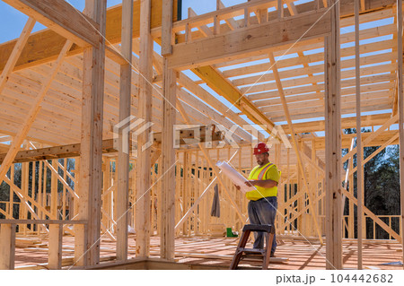 An engineer checking quality of wooden frame using blueprint plan architecture during construction phase project 104442682