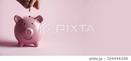 Hand puts a coin in a piggy bank. 104444299