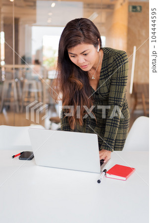 Focused woman browsing laptop at desk Focused woman browsing laptop at desk 104444595