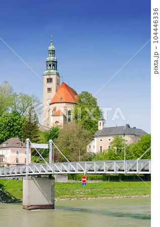 Muelln, a neighborhood in Salzburg, Austria. Pedestrian bridge Muellner Steg over Salzach river, a connection to the right old town of Salzburg. On the hill Muelln Church, the Catholic parish church. Muelln, a neighborhood in Salzburg, Austria. Pedestrian bridge Muellner Steg over Salzach river, a connection to the right old town of Salzburg. On the hill Muelln Church, the Catholic parish church. 104446336