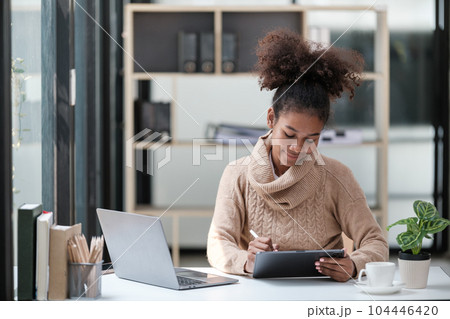 American African Woman working in the office with computer phone and Tablet. American African Woman working in the office with computer phone and Tablet. 104446420