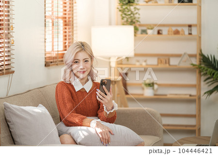 Young asian woman using a smart phone sitting on the sofa in the room. Order some online shopping. Young asian woman using a smart phone sitting on the sofa in the room. Order some online shopping. 104446421