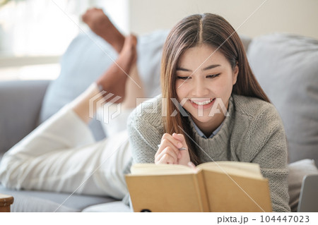 Asian woman woman reading book on sofa in living room. Asian woman woman reading book on sofa in living room. 104447023