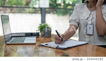 Happy young asian woman talking on the mobile phone and while sitting at working place in office Happy young asian woman talking on the mobile phone and while sitting at working place in office 104448392