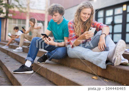Teenage friends boy and girl holding phones and browsing 104448465