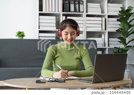 Young beautiful Happy Asian woman using laptop taking notes at home 104448486
