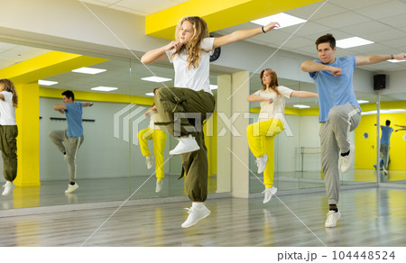 Flexible and energetic male and female teenage dancers jumping and having fun during dance training in hall 104448524