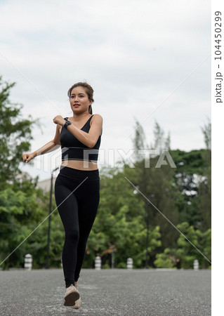 Happy woman wearing sportswear jogging in the park. Young beautiful asian female in sports bra running outdoor. Workout exercise in the morning. Healthy and active lifestyle concept 104450299