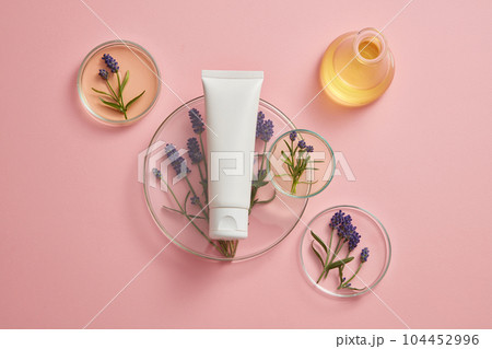 Pastel background for advertising with minimalist concept. An empty plastic tube decorated with fresh lavender and petri dishes containing yellow liquid. Cosmetic mockup with lavender extract. 104452996