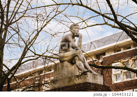 a statue sitting on top of a stone block in front of a brick building with trees and sky in the background 104453121