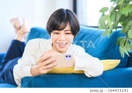 ソファーに寝そべる若い女性　リビング　スマホ 104453241