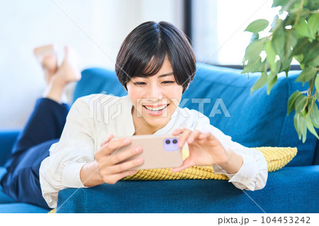 ソファーに寝そべる若い女性 リビング スマホ ソファーに寝そべる若い女性 リビング スマホ 104453242