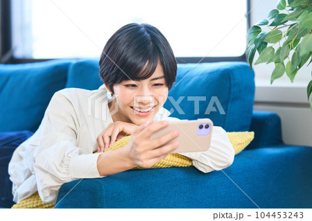 ソファーに寝そべる若い女性 リビング スマホ ソファーに寝そべる若い女性 リビング スマホ 104453243