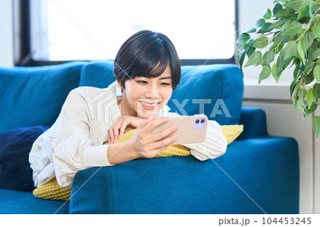 ソファーに寝そべる若い女性　リビング　スマホ 104453245