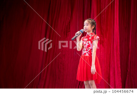 The Asian kid girl sing a song on stage at her school activity day, dress in Qipao style, red curtain background 104456674