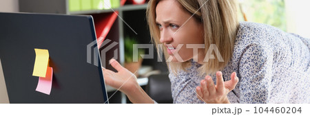 Upset woman looking at laptop screen with angry expression Upset woman looking at laptop screen with angry expression 104460204
