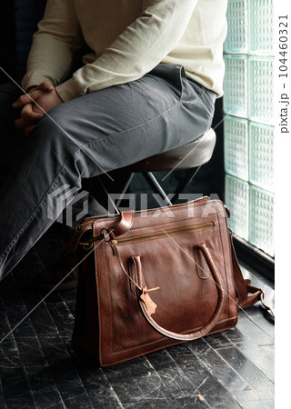 close-up photo of light brown leather briefcase on a black wooden floor. 104460321