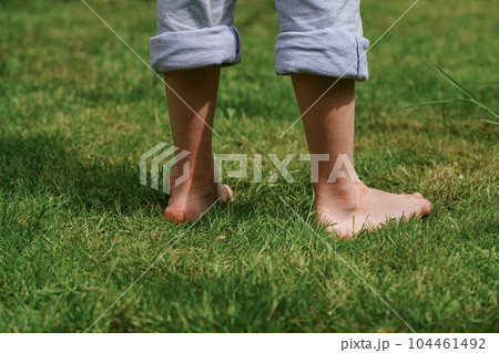 A happy child standing barefoot on the grass, close-up of the feet. Sunny summer day. Summer Vacation 104461492