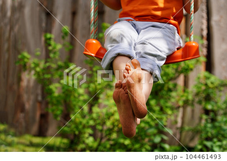Boy crossed his bare feet. Closeup of feet happy kid sitting and swinging, sunny summer day, countryside background. Child feet barefoot. 104461493