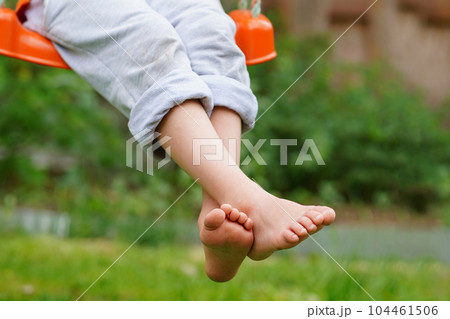 Boy crossed his bare feet. Closeup of feet happy kid sitting and swinging, sunny summer day, countryside background. Child feet barefoot. 104461506