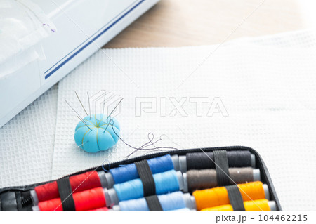 Sewing layout with multicolored spools of thread close-up, needles, electric sewing machine. Filling the thread into the sewing needle, adjusting the tension. hobby, home business 104462215