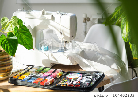 Sewing layout with multicolored spools of thread close-up, needles, electric sewing machine. Filling the thread into the sewing needle, adjusting the tension. hobby, home business 104462233