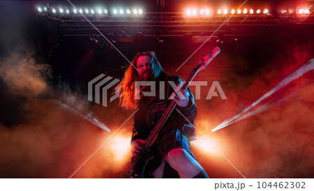 Rock and roll concert. Artistic, expressive man with long hair playing guitar and making performance, emotionally singing 104462302