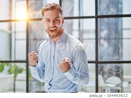 Portrait of a young businessman in a blue shirt shaking his fists celebrating his success 104463612