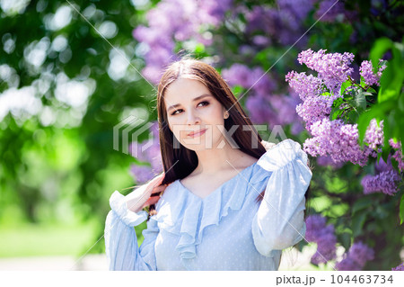 pretty girl with long hair stands with lilac flowers, in the garden 104463734