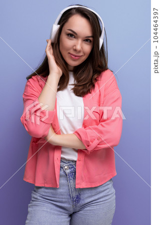 smiling brunette lady with dark hair below her shoulders in a shirt and jeans listens to music in 104464397