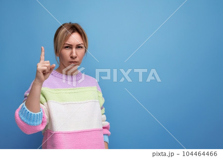cute blond woman in casual look pointing finger at copy space wall on blue background 104464466