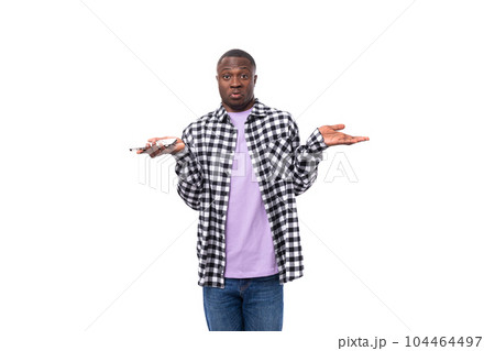 a confused 30 year old african guy dressed in a plaid black and white shirt shrugs his shoulders 104464497