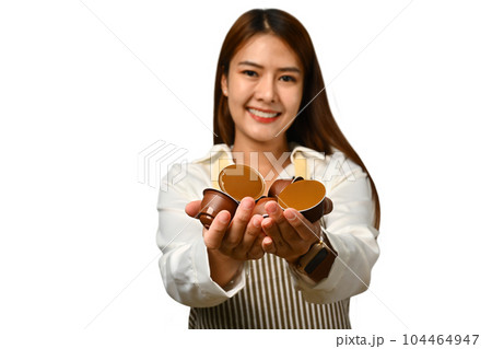 Beautiful young woman wearing apron hands holding coffee capsules isolated on white background 104464947