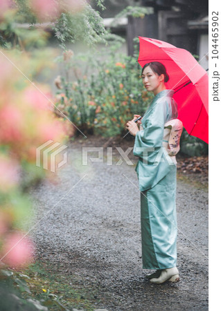 自然溢れる景色の中赤い傘をさし趣のある表情をしている和服の若い女性 104465902