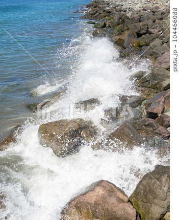 Waves with splashes fall on large stones. Shore view. Beautiful stones that strengthen the shore from the surf. Powerful coastline. Sea foam. The excitement of the sea. Waves with splashes fall on large stones. Shore view. Beautiful stones that strengthen the shore from the surf. Powerful coastline. Sea foam. The excitement of the sea. 104466088