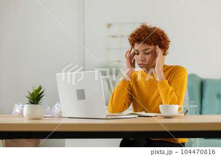 African woman touching temples experiencing stress. Girl at home office tired of working feeling headache sick rubbing temples forehead. Long laptop usage computer vision syndrome. Office syndrome 104470816