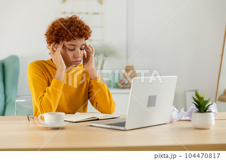 African woman touching temples experiencing stress. Girl at home office tired of working feeling headache sick rubbing temples forehead. Long laptop usage computer vision syndrome. Office syndrome 104470817
