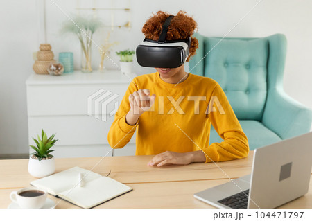 African american young woman wearing using virtual reality metaverse VR glasses headset at home. Girl touching air during VR experience on virtual reality helmet. Simulation hi-tech videogame concept African american young woman wearing using virtual reality metaverse VR glasses headset at home. Girl touching air during VR experience on virtual reality helmet. Simulation hi-tech videogame concept 104471797