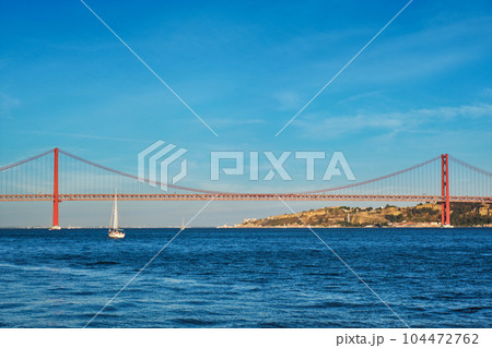 View of 25 de Abril Bridge famous tourist landmark over Tagus river and a tourist yacht boat at sunset. Lisbon, Portugal View of 25 de Abril Bridge famous tourist landmark over Tagus river and a tourist yacht boat at sunset. Lisbon, Portugal 104472762